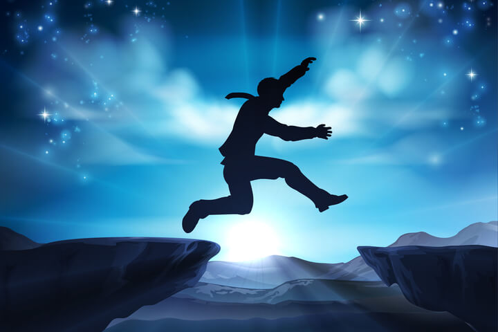 A person jumping across a gap between two cliffs