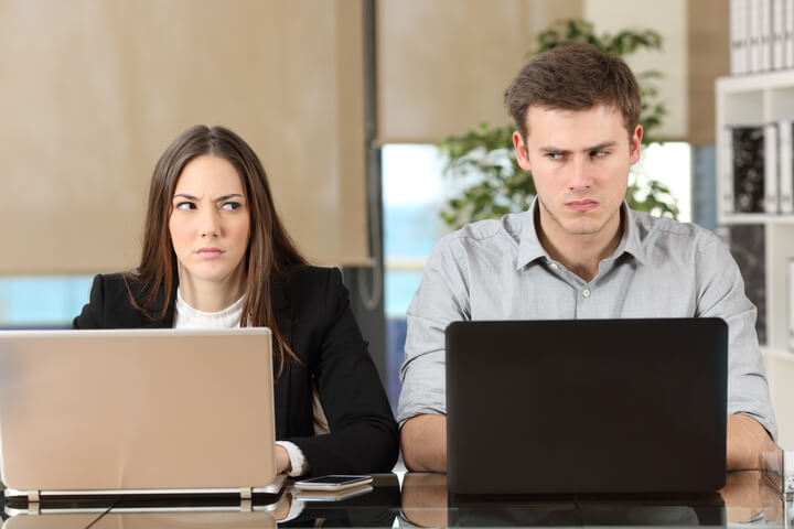 Two coworkers looking at each other with disgust