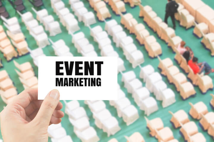 A person holding up a sign saying "Event Marketing" overtop of an image of a bunch of chairs lined up at an event
