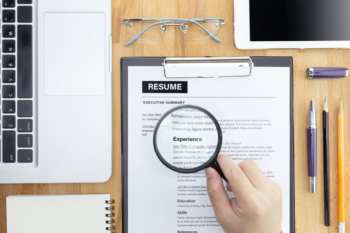 A person using a magnifying glass to look at a resume
