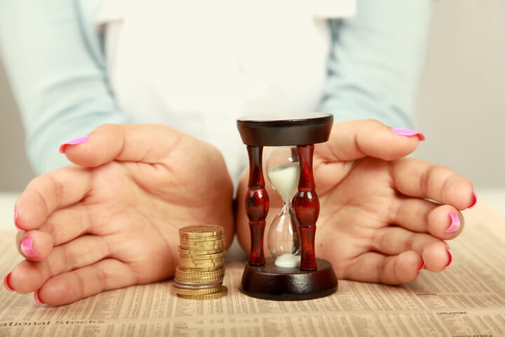 A person's hands surrounding a stack of change and an hourglass