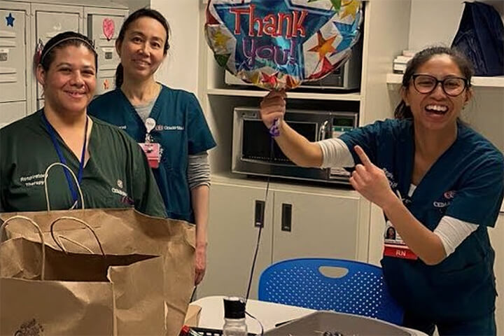 three frontline health workers with one holding a balloon that says thank you